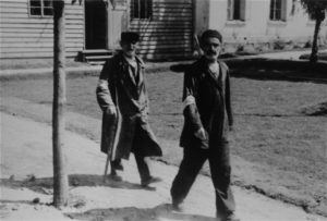 Two Jewish men wearing armbands walk along a path in Konskowola